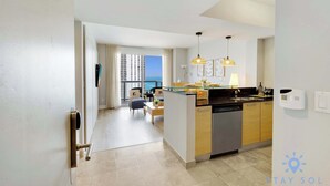 A modern kitchen with a dishwasher, a dining area with a table and chairs, and a view of the ocean through large windows. - 1BR Apartment with beautiful view (Sunny Isles Beach)