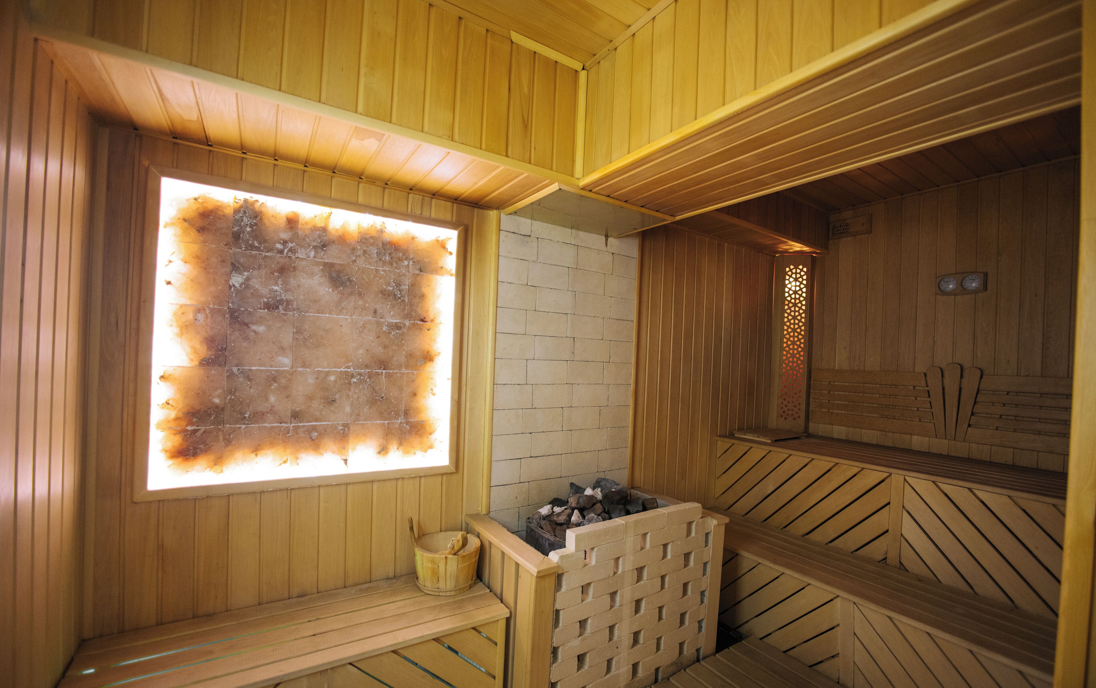 A sauna with wooden walls, a brick wall section, a window with a burnt pattern, and a wooden bench.