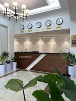 Una zona de recepción con un mostrador de madera, varios relojes de pared y plantas en macetas.