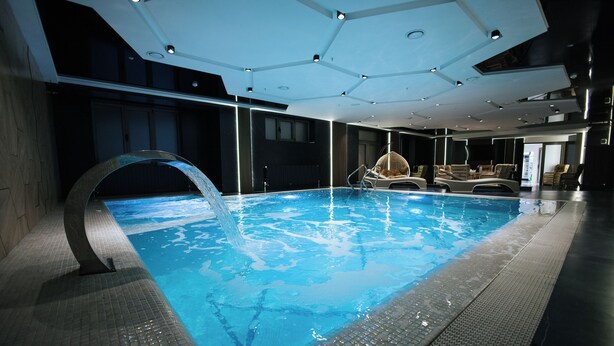 Ein moderner, überdachter Pool mit klarem Wasserspiel, umgeben von Liegestühlen und einem zeitgemäßen Deckenstil.