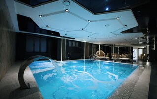 Una piscina interior con diseño moderno, que incluye una estructura de techo única y un área de descanso con sillas.