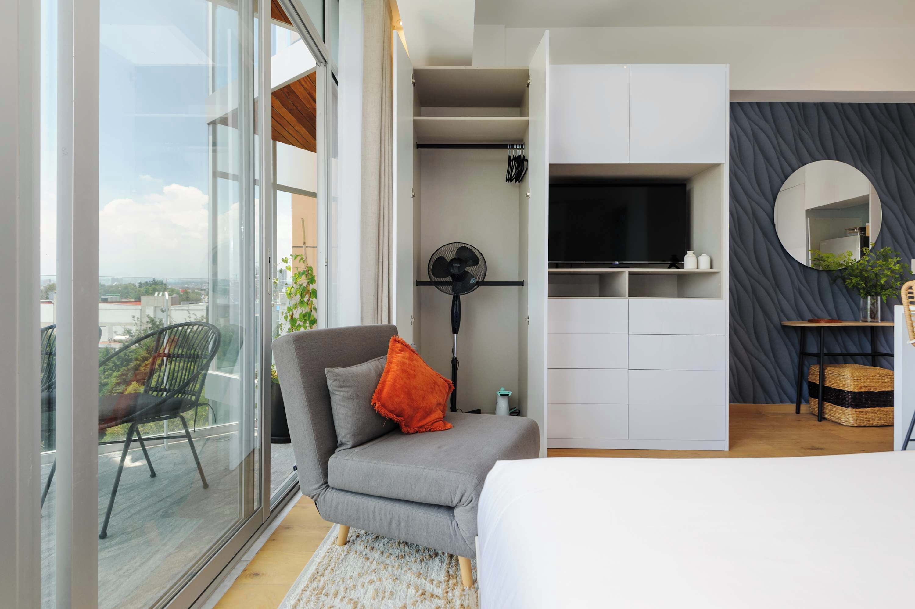 Une chambre moderne avec un canapé gris, une petite table, un miroir et un téléviseur.