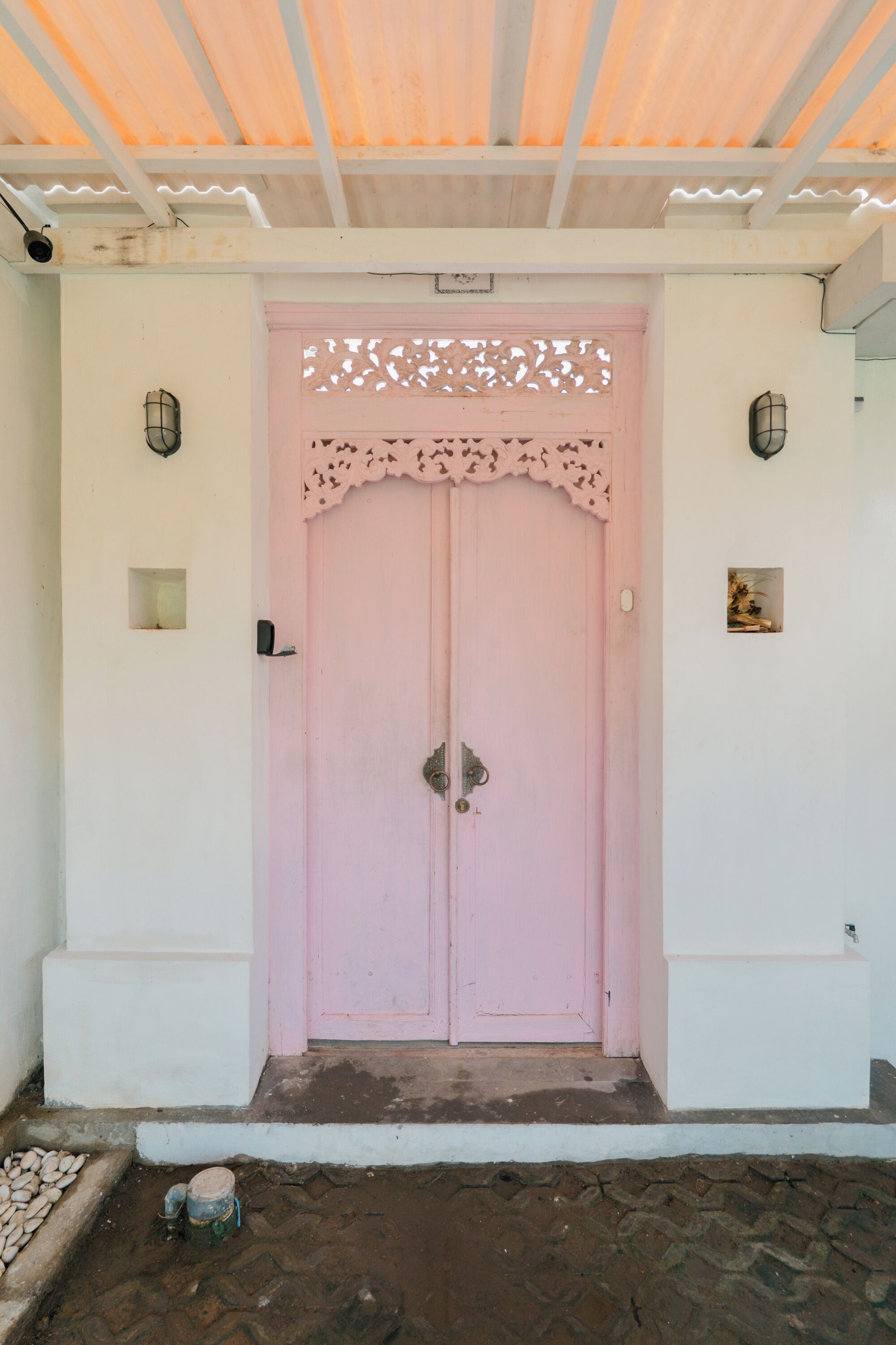 A pink door with a decorative upper section, a white wall, and a small square window on the right.