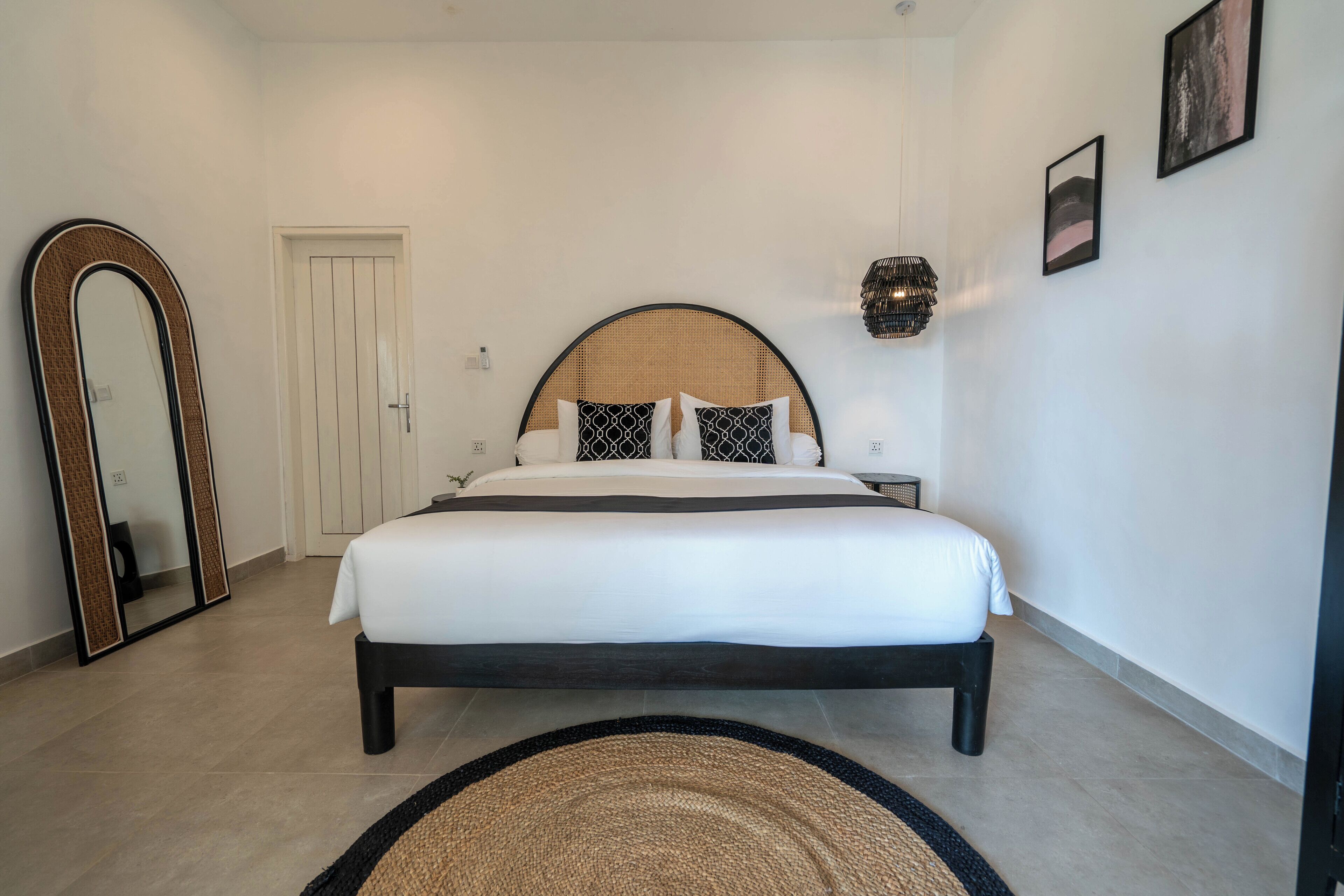 Quarto com cama, espelho grande, porta e luminária fixada na parede.