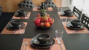 Mesa de jantar posta com pratos, tigelas e talheres pretos, com uma fruteira no centro.