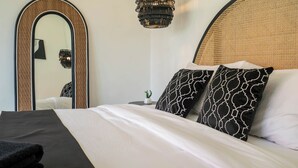 Uma cama bem arrumada com almofadas estampadas, um espelho grande e um lustre pendente.
