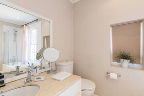 Une salle de bain avec un lavabo, un miroir, des toilettes et une fenêtre avec une plante.