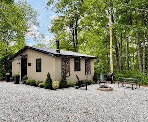 Une petite cabane avec une allée en gravier, un foyer et des sièges d’extérieur.