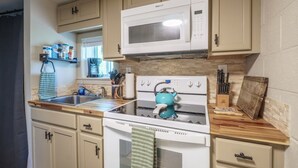 A kitchen with beige cabinets, a white microwave, a stove with a teal kettle, and a wooden countertop.