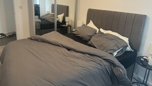 Een slaapkamer met een groot bed, een nachtkastje met een lamp en een spiegel.