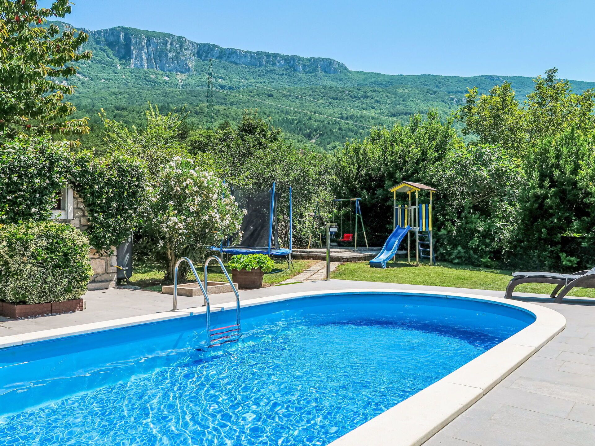 A swimming pool with a view of a playground and mountains in the background.