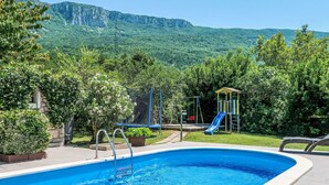 Une piscine avec vue sur une aire de jeux et, au loin, sur des montagnes.