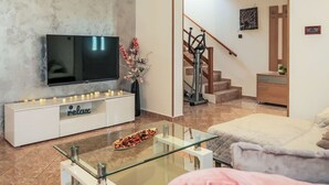 Un salon moderne doté d’un téléviseur à écran plat, d’une table basse en verre, d’un canapé et d’un escalier menant à l’étage supérieur.