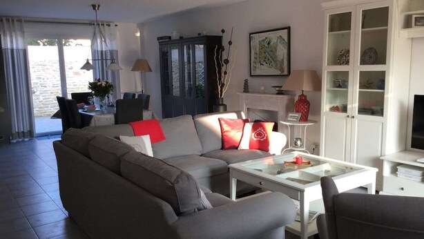 Ein modernes Wohnzimmer mit einem grauen Sofa, einem weißen Couchtisch und einem Fernseher. Es gibt ein Schränkchen mit Glastüren und ein Bild an der Wand.