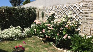 Ein Garten mit verschiedenen blühenden Pflanzen, einer Steinmauer und einer weißen Gitterstruktur.