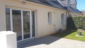 Ein Haus mit einer Schiebetür, einem kleinen Fenster und einem Garten mit Rasenfläche und einem Blumentopf.