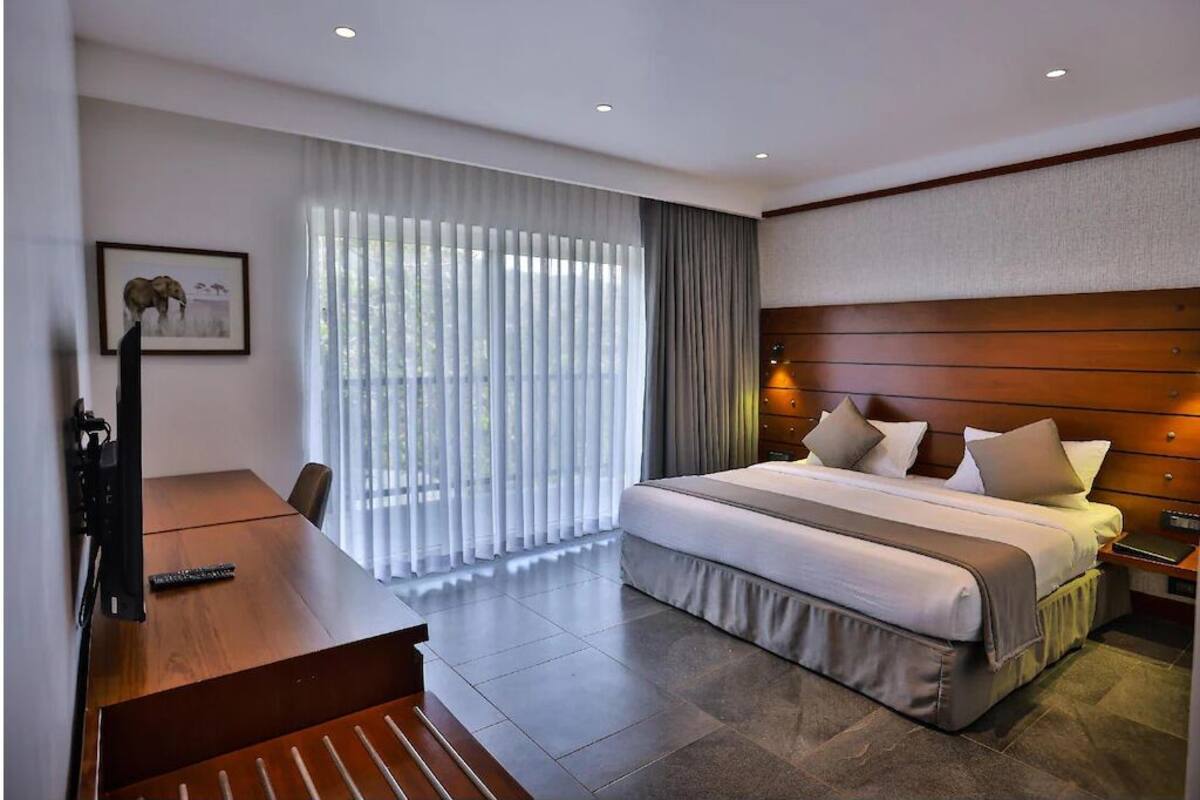 Habitación de hotel con una cama grande, un escritorio y una silla. Hay una ventana con cortinas y un cuadro en la pared.