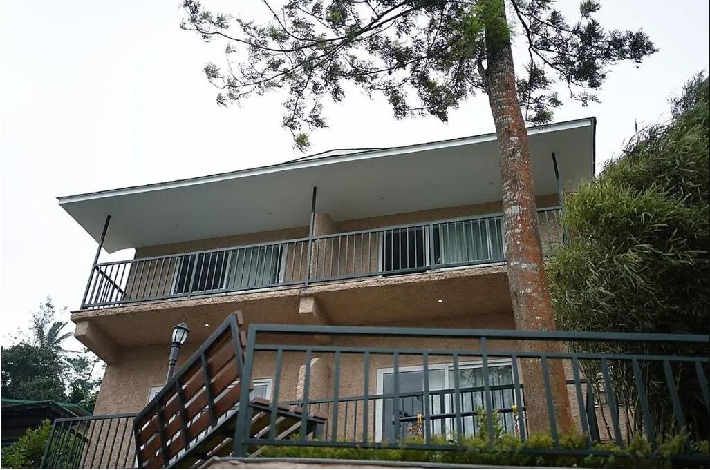 A two-story building with a flat roof, a balcony on the upper floor, and a staircase leading to the entrance.