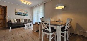 Un salon chaleureux avec un canapé, une table à manger et des chaises, un tableau accroché au mur et une fenêtre avec des rideaux.