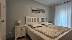 Makuuhuoneessa on yksi sänky, yöpöytä, lamppu, seinällä taulu ja ikkuna, jossa on verhot.