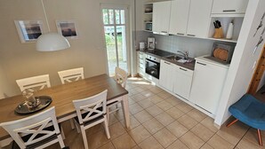Moderni keittiö, jossa on valkoiset kaapit, ruokailutila puupöydällä ja valkoisilla tuoleilla sekä sininen tuoli nurkassa.