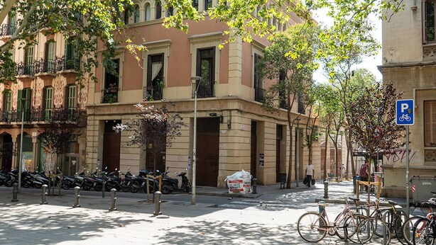 Una calle con bicicletas y motocicletas estacionadas, un edificio con fachada tradicional, y un cielo azul despejado.