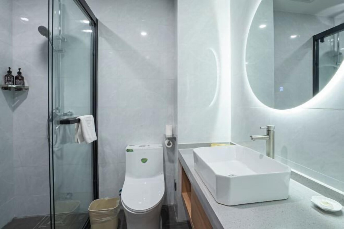 A modern bathroom with a glass-enclosed shower, a white toilet, a rectangular sink, and a round mirror.