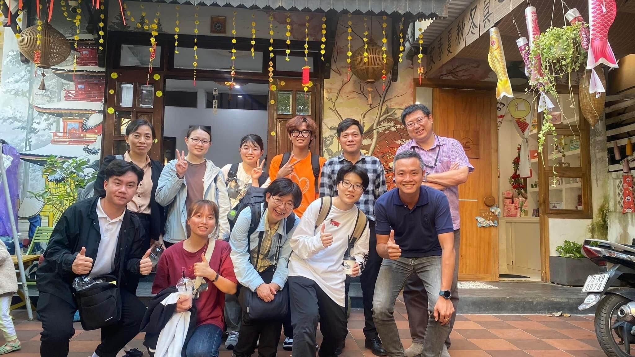 A group of people posing in front of a building with traditional architecture, including a wooden door and hanging decorations.