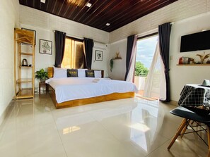Un dormitorio amplio con una cama grande, un armario de madera, una mesita pequeña y un balcón con cortinas.
