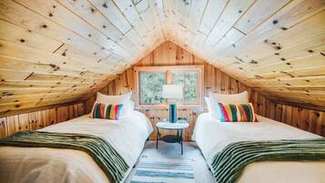 A cozy attic bedroom with two beds, a window, and a lamp.