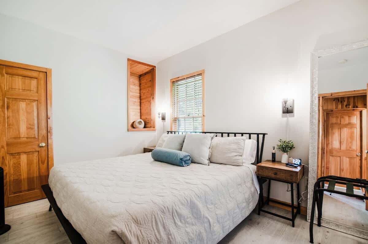 A bedroom with a bed, a nightstand, a window, and wooden doors.