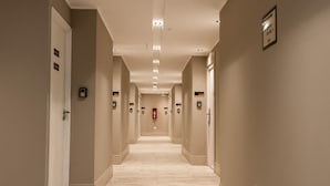 A long, narrow hallway with beige walls and a light-colored floor, featuring doors with numbered signs and a fire alarm on the wall. - Triple apartment one block from the Main Sq. (Salta)