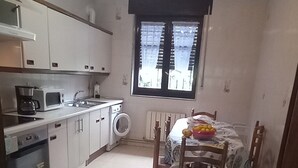 Cocina compacta con armarios blancos, un microondas, un lavamanos y un comedor con mesa y sillas.