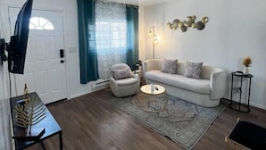 A living room with a sofa, armchair, coffee table, and a TV on a stand.