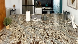 A modern kitchen with granite countertops, stainless steel appliances, pendant lighting, and a backsplash with black tiles.