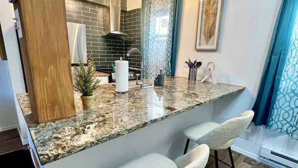 A modern kitchen with a granite countertop, two bar stools, a hanging light fixture, and a backsplash with a geometric pattern.