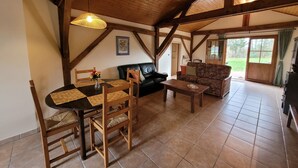 A rustic interior with a wooden ceiling, a dining table with chairs, a sofa, and a patterned couch.