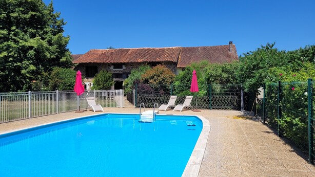 A swimming pool with lounge chairs and umbrellas, surrounded by a fence and trees.