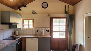 A compact kitchen with a dishwasher, stove, and a window with a curtain.