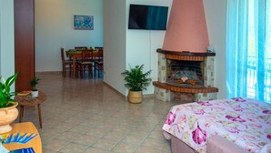 A room with a fireplace, a dining area, a TV mounted on the wall, and a bed with a floral bedspread. - Casa Tramonti D Amare - On the Hills of the Amalfi Coast (Tramonti)