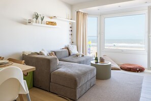 A modern living room with a sofa, a dining table, and a view of the beach. - 3 bedroom accommodation in Wenduine (Wenduine)