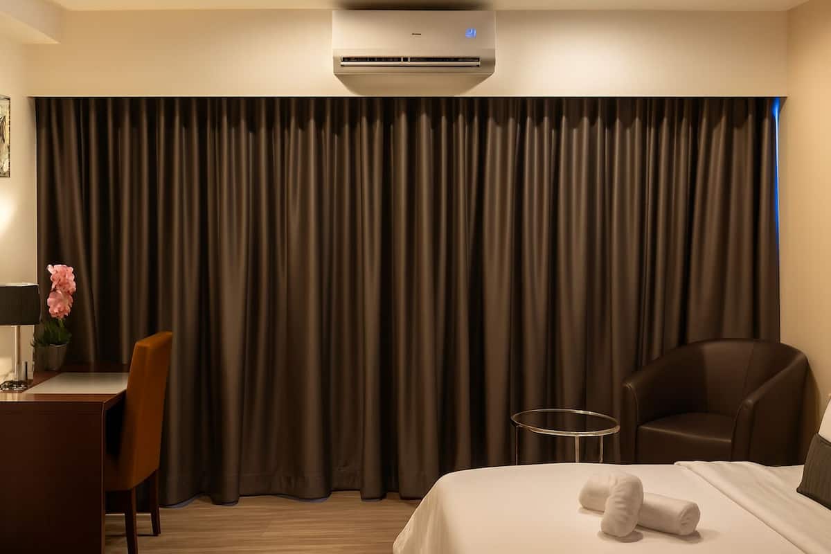 A hotel room with a bed, a desk with a chair, a small table, and a large curtain.