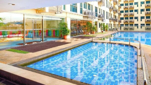 Una piscina con suelo de baldosas, rodeada por un edificio con balcones y fachada de vidrio.