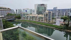 Un edificio moderno con fachada de vidrio, un río al frente y un puente en el fondo.