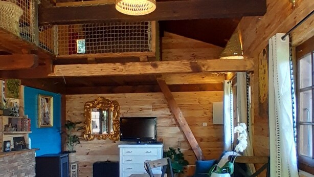A rustic wooden interior with a dining area, a television on a dresser, and a balcony with string lights.