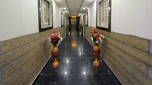 Un pasillo con paredes de mármol y suelo negro, con dos jarrones decorativos con flores.