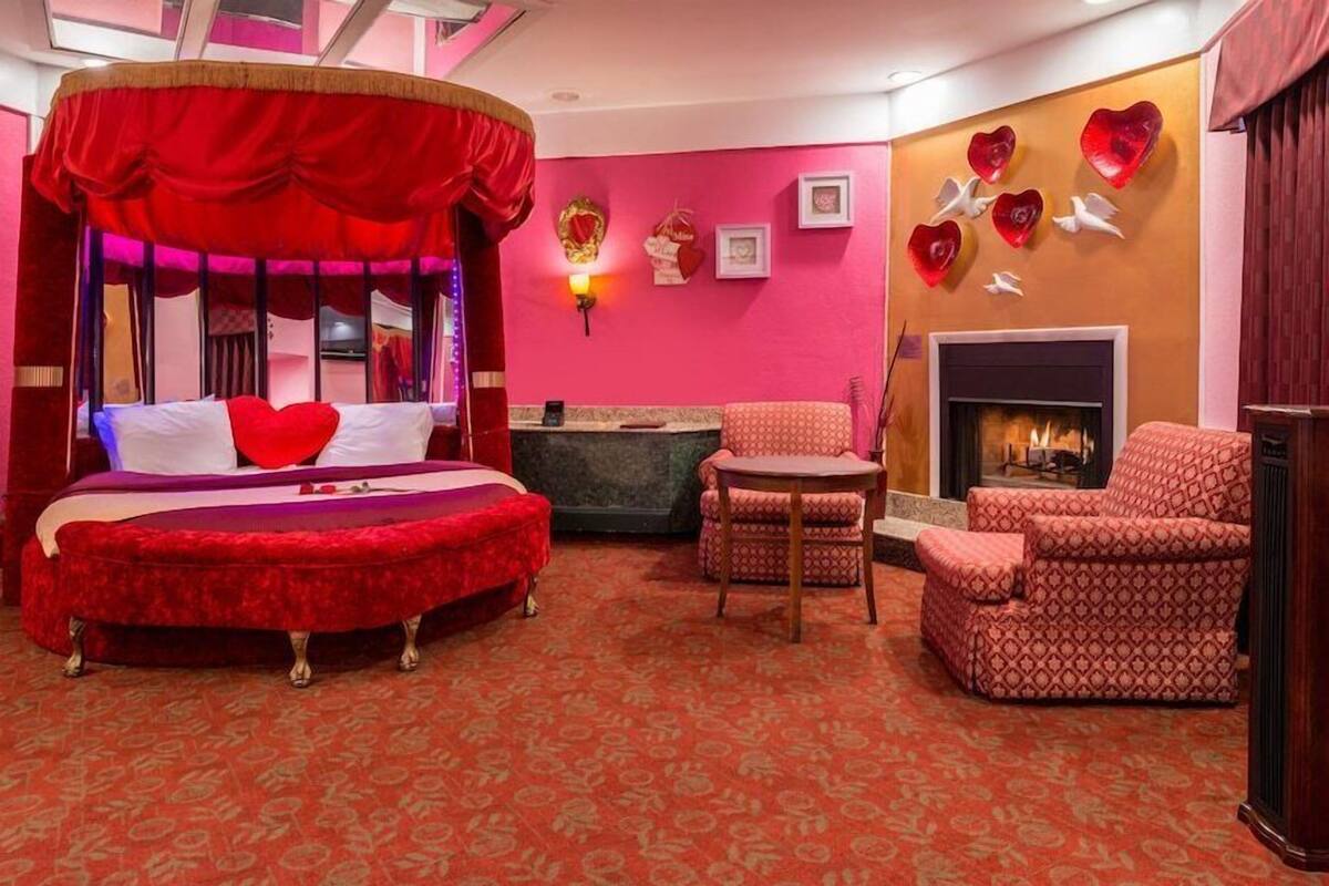 A room with a four-poster bed, a fireplace, a red patterned carpet, and heart-shaped wall decorations.