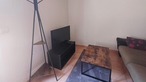 Huoneessa on puinen sohvapöytä, musta kaappi, lattiavalaisin ja kuviollinen koristetyynyillä varustettu sohva.