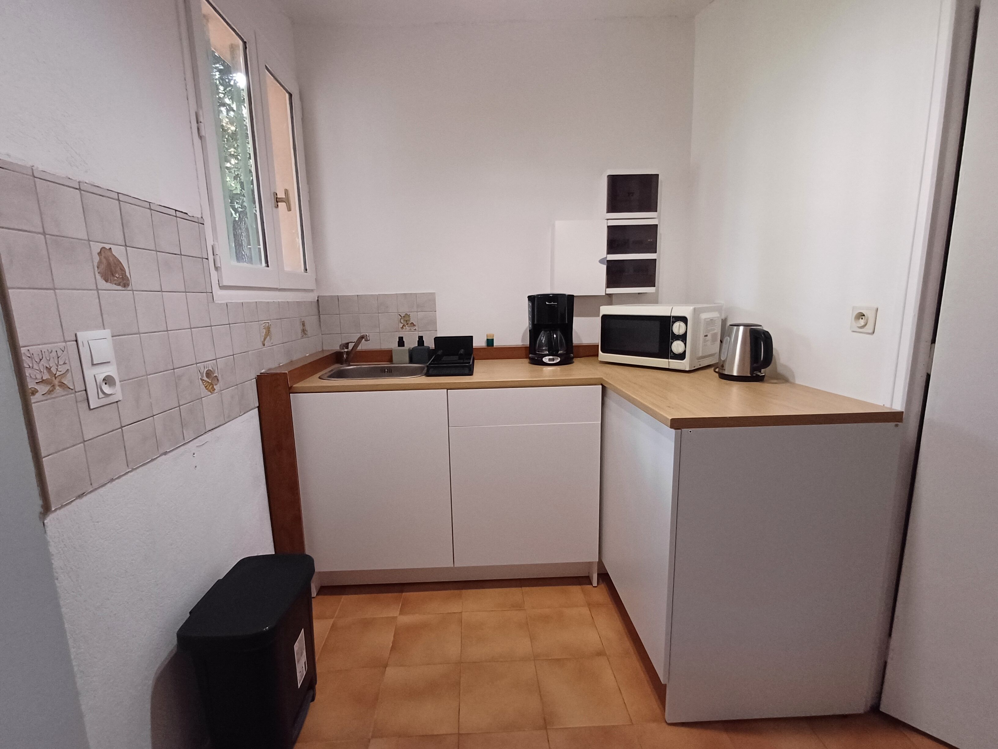 A compact kitchen with white cabinets, a sink, a coffee maker, a microwave, and a toaster.