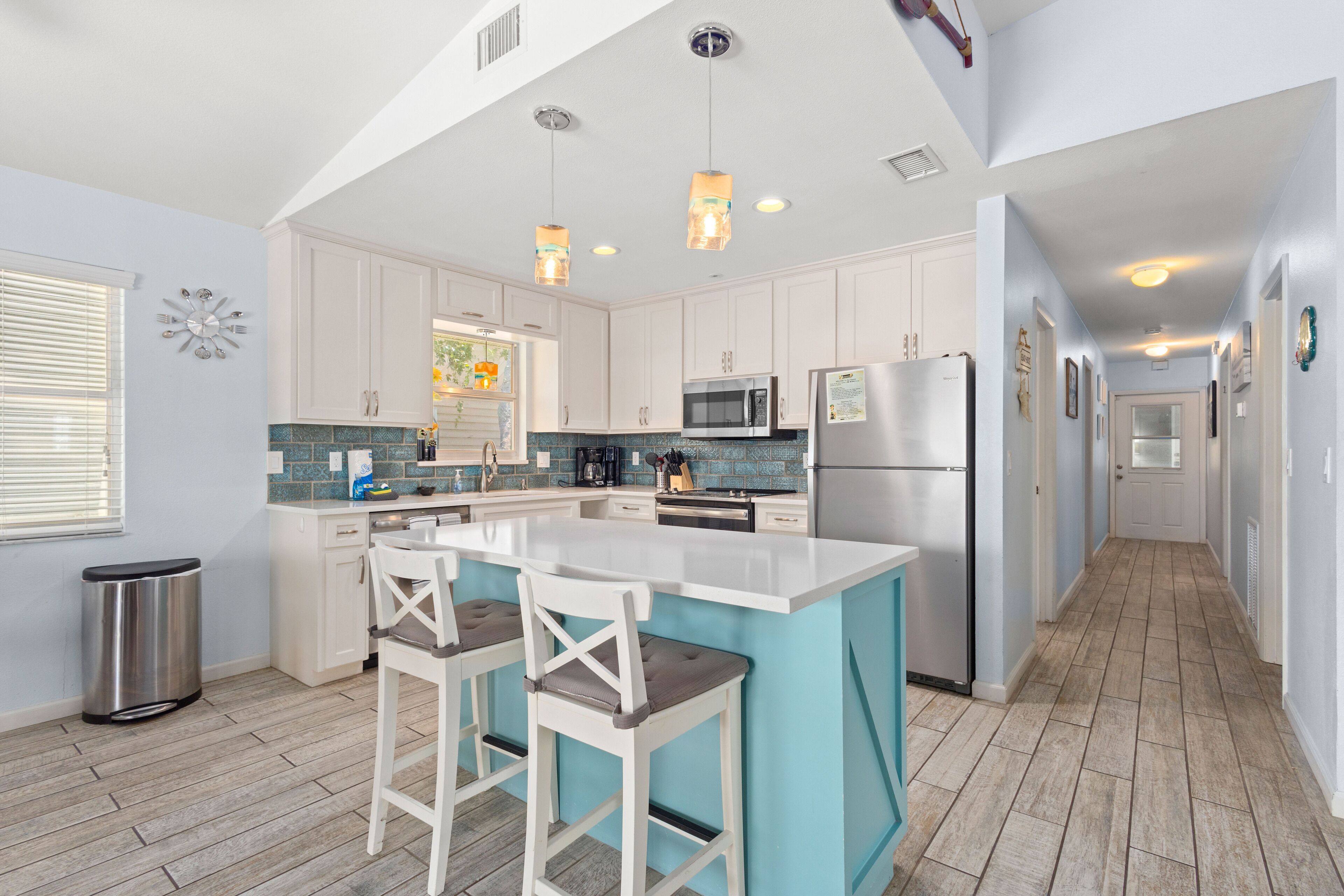A modern kitchen with white cabinets, a large island with bar stools, stainless steel appliances, and a blue backsplash.